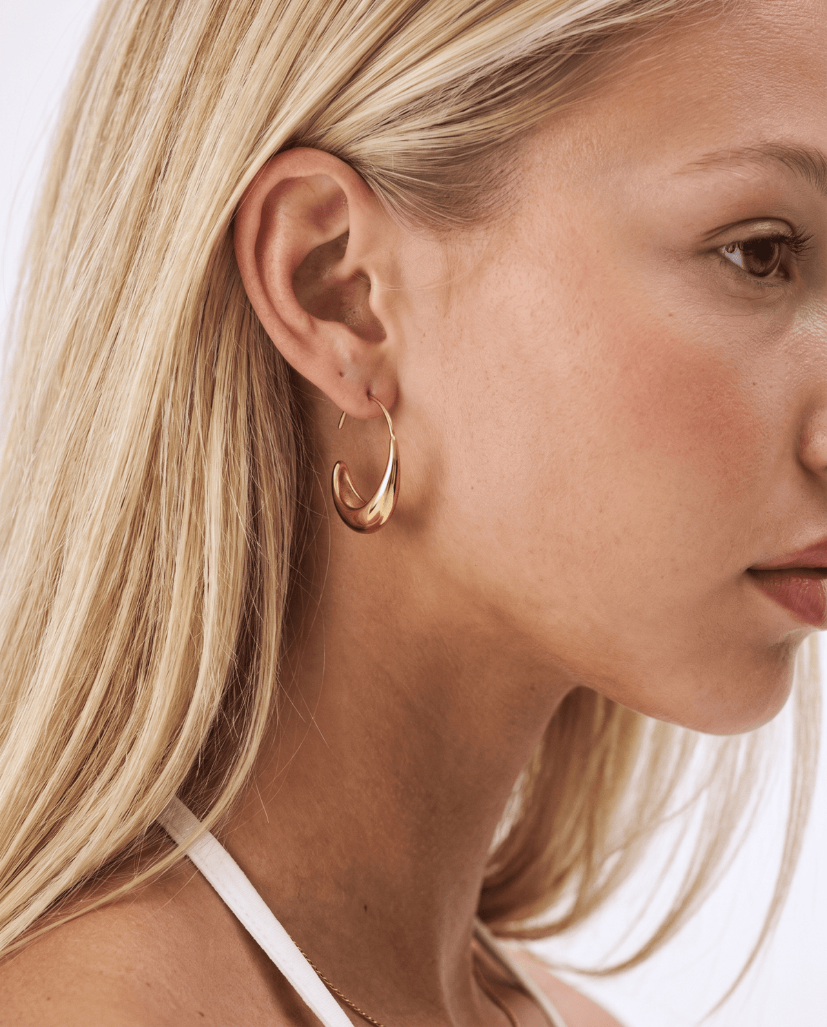 Gold hoop earrings with teardrop design worn on the ear