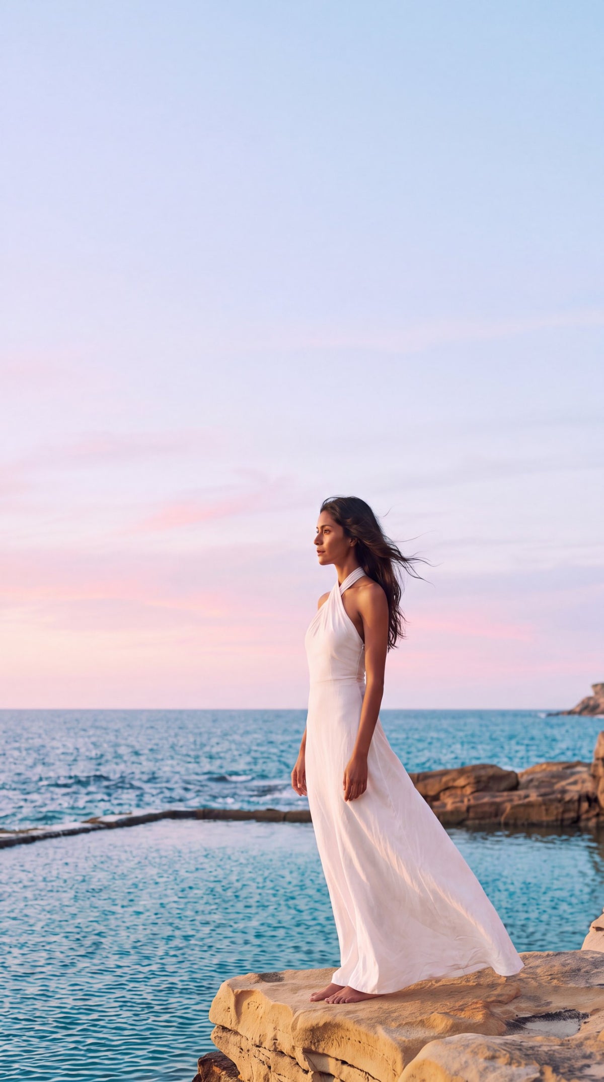 Woman in a white halter maxi dress by the sea at sunset